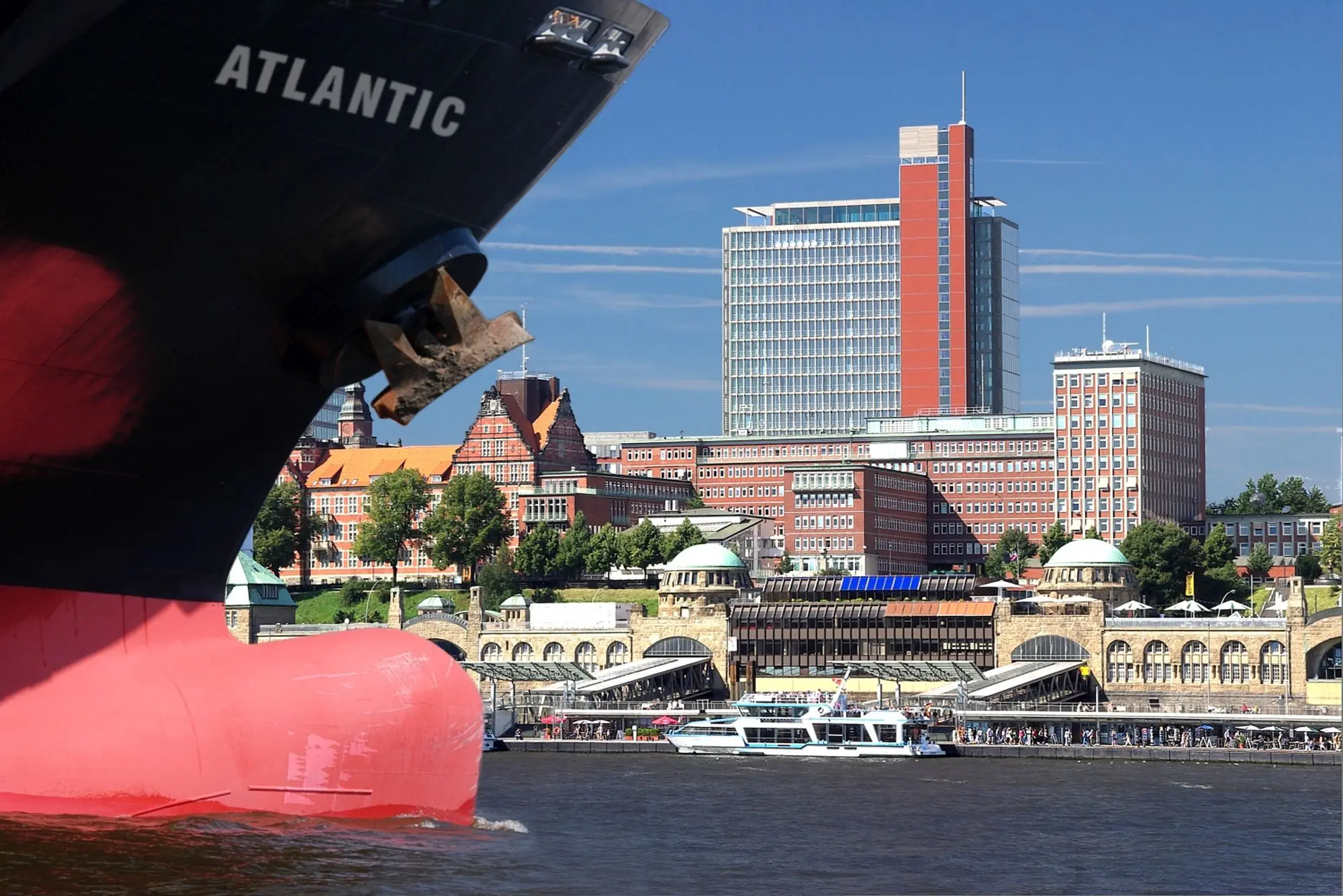 Blick auf das Atlantic-Haus in Hamburg-St. Pauli mit Elbe, Landungsbrücken und vorbeifahrendem Schiff.
