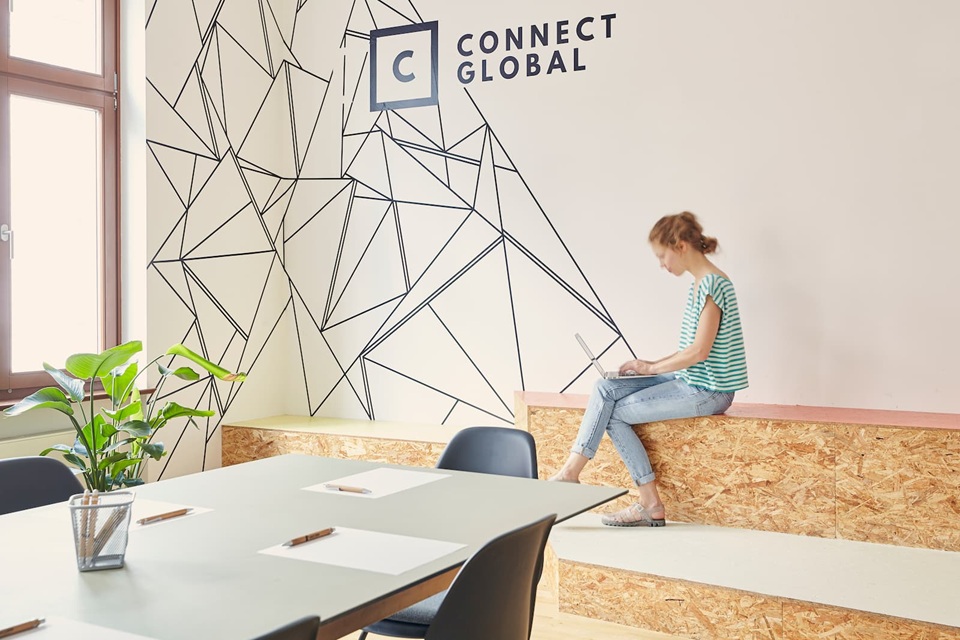Moderne Arbeitsumgebung mit kreativem Wanddesign, flexiblen Sitzbereichen und junger Mitarbeiterin am Laptop im Büro von Connect Global in Hamburg.