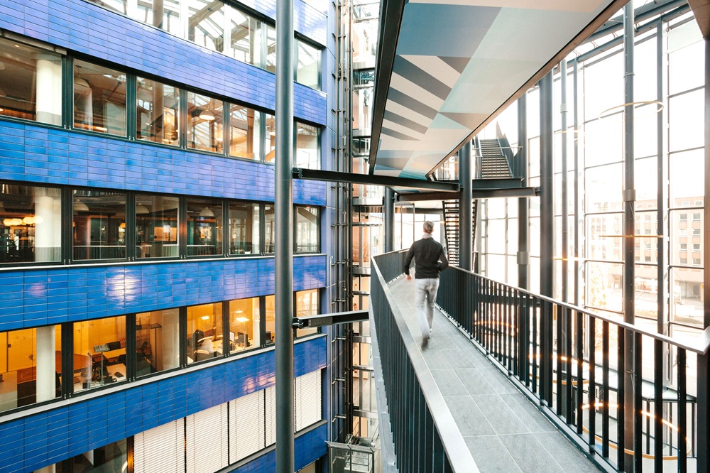Glasüberdachter Bürokomplex von WeWork Hamburg mit offener Galerie, modernen Arbeitsplätzen und lichtdurchflutetem Atrium – Sinnbild für neue Arbeitswelten.